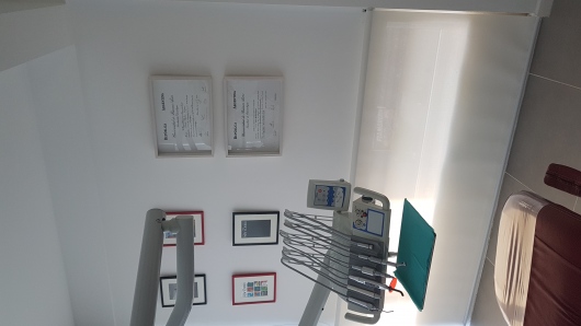 Modern bright dental clinic interior with an ergonomic sleek white and teal dental chair, high-tech dental examination equipment, clean clinical lighting, wooden and teal accents, minimalist aesthetic, professional photography, warm welcoming medical office in Buenos Aires, sharp focus, 8k